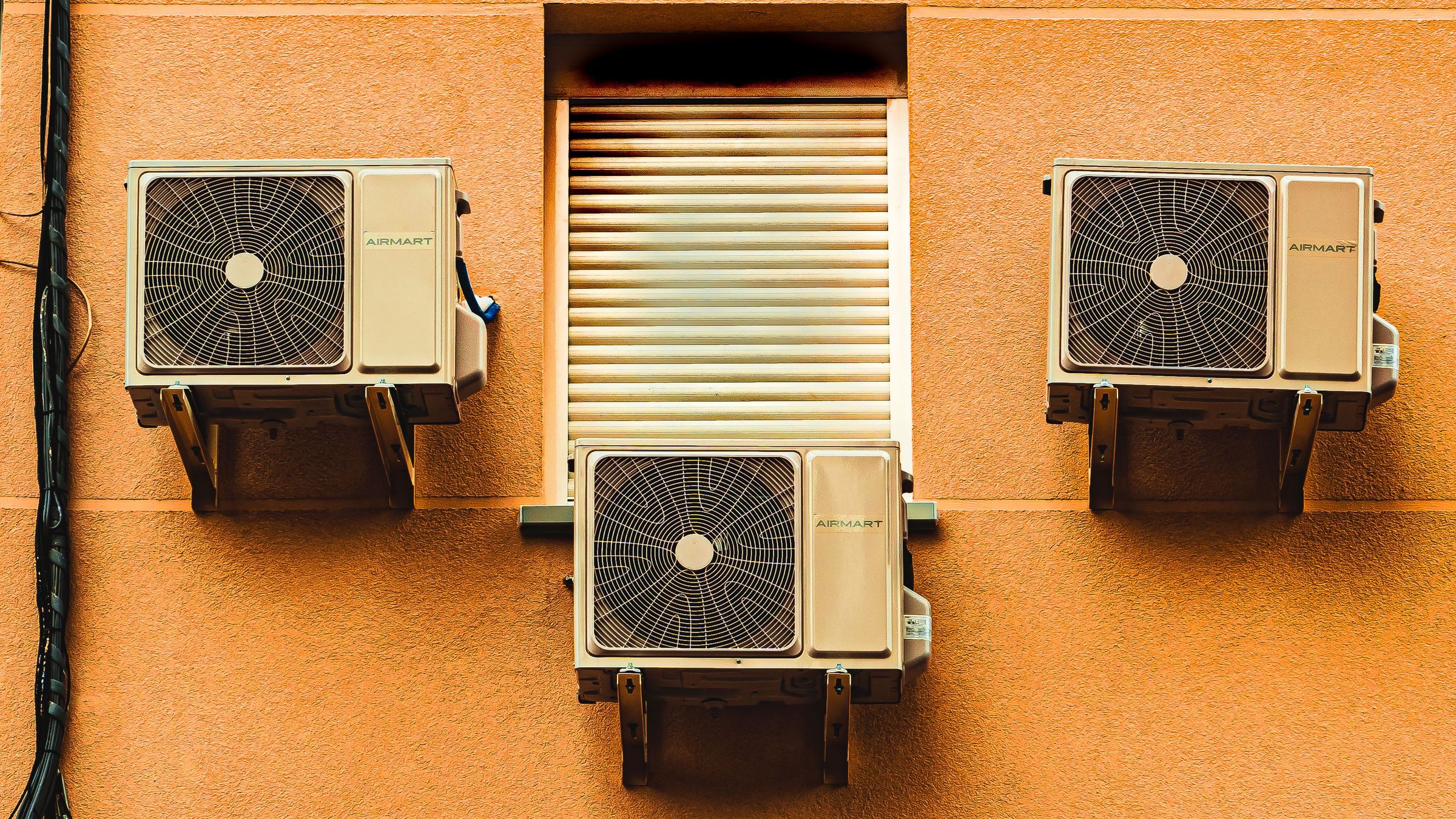 Three air conditioning condenser units mounted on an orange building wall