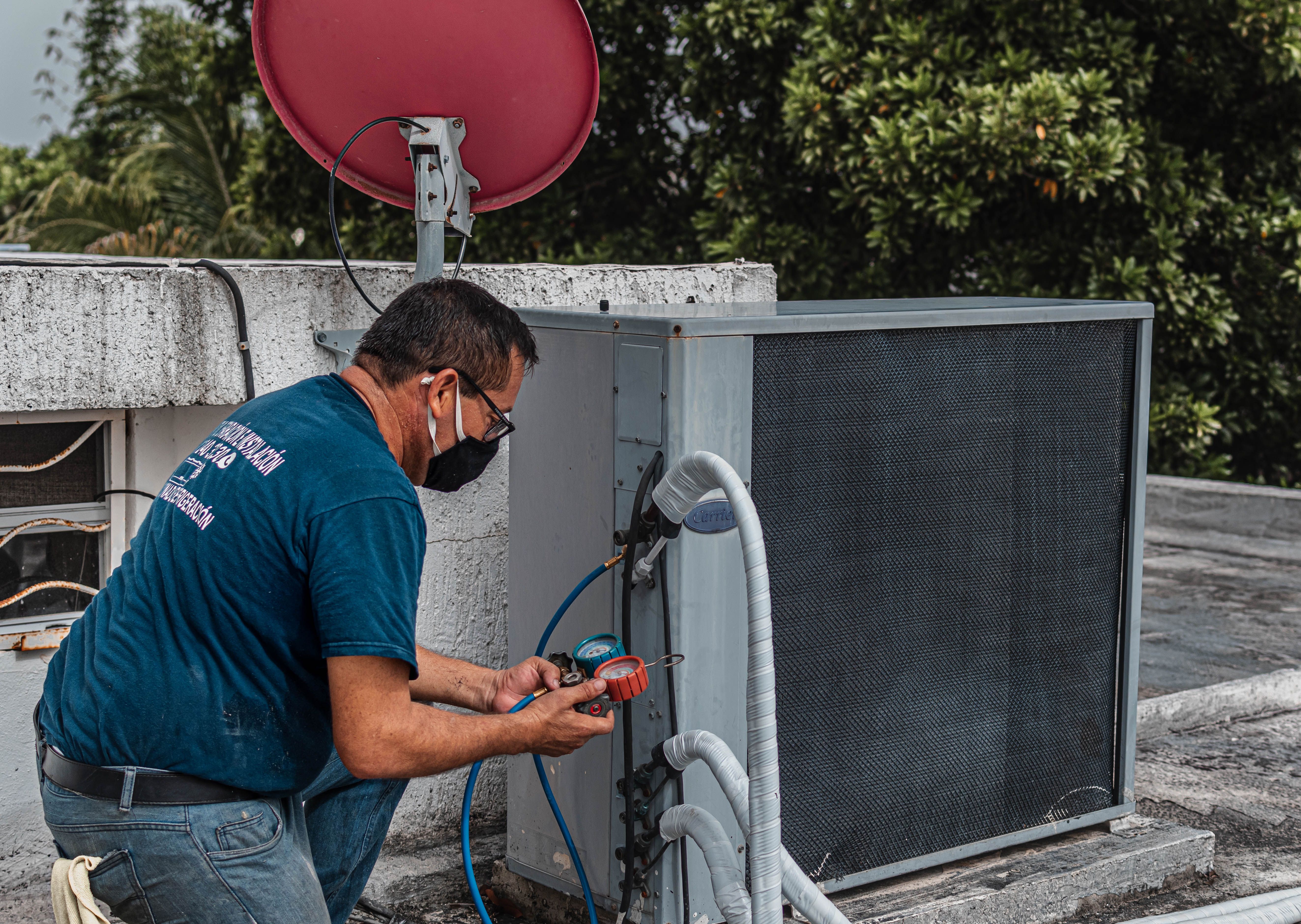HVAC technician kneeling at a rooftop condenser unit, checking refrigerant pressure with a gauge manifold