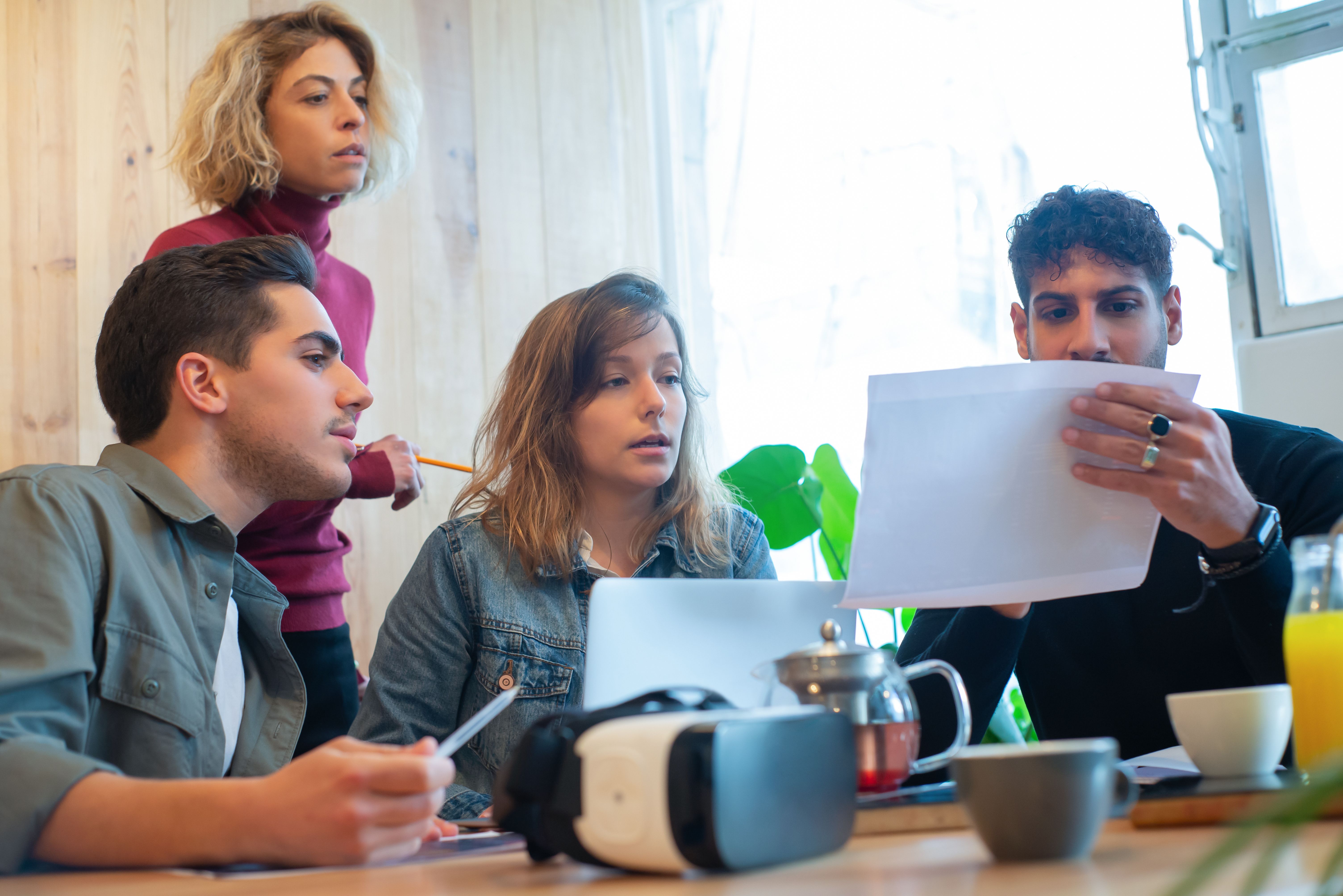 A small team gathered around a laptop reviewing printed performance results together
