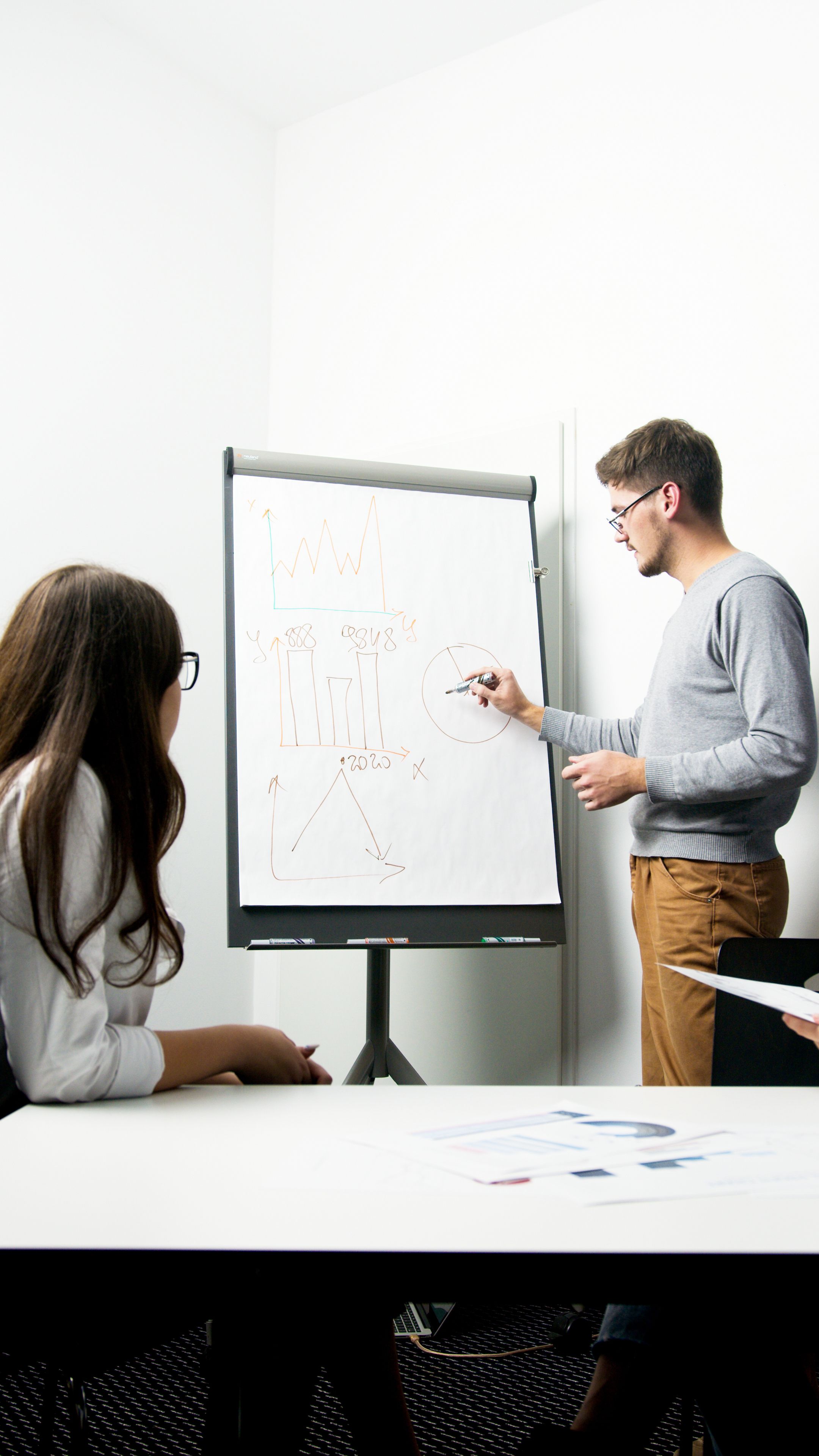 Two marketers reviewing campaign performance charts on a whiteboard during a strategy session